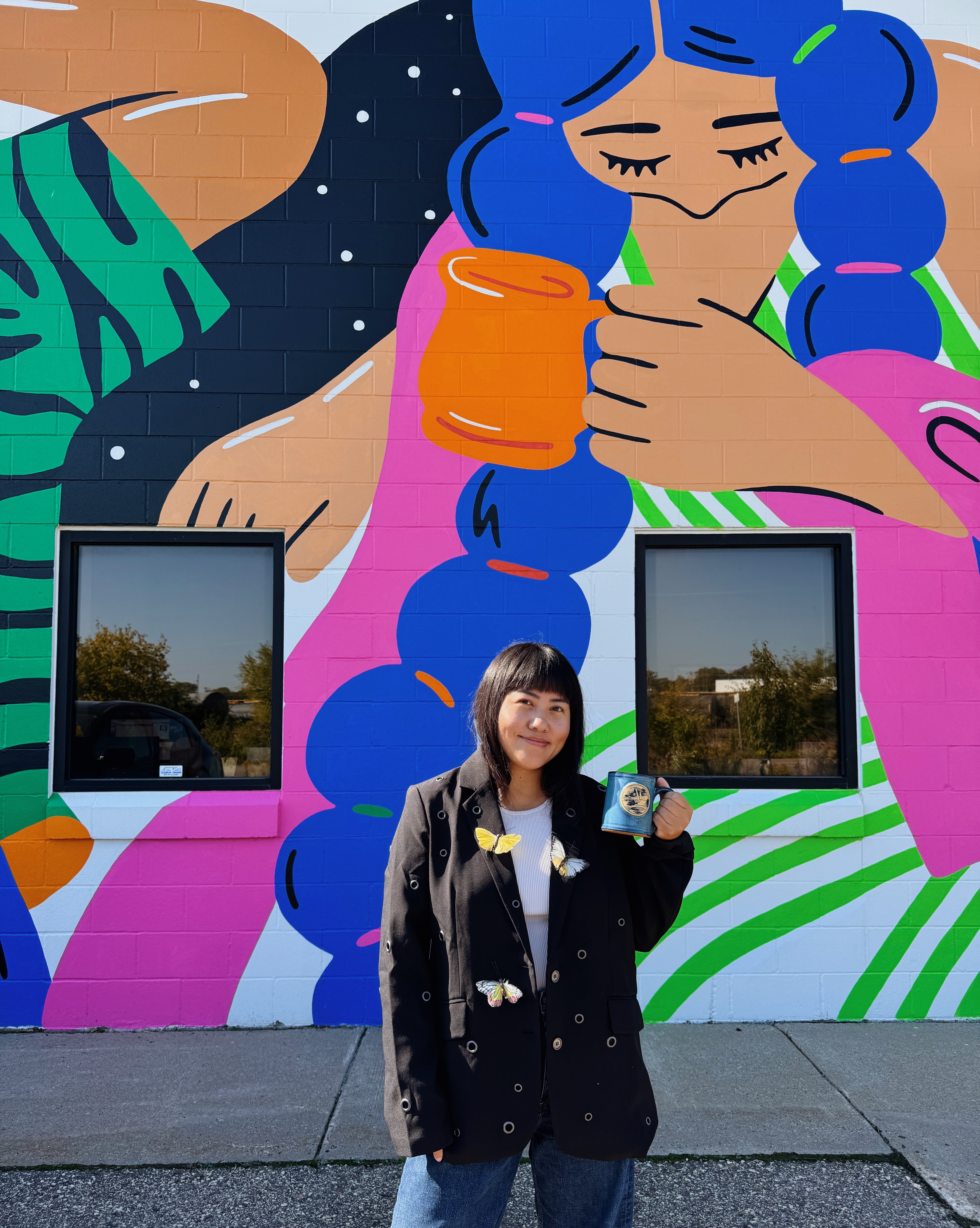 Christina holding her illustrator mug in front of her mural 